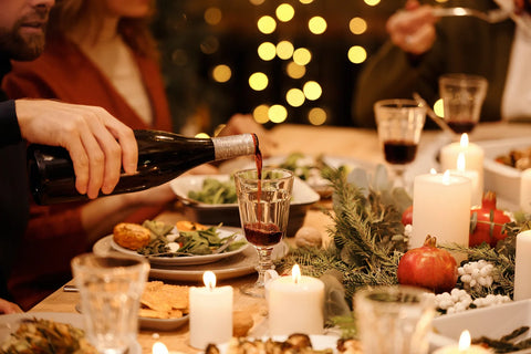 a man pouring red wine to his glass on a crowded table